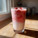 A tall glass of layered strawberry milk with a frothy, bright red top layer and white milk at the bottom.