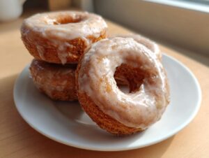A stack of four moist baked pumpkin donuts covered in a light cinnamon glaze, sitting on a white plate.