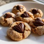A plate of freshly baked peanut butter blossom cookies, coated in sugar and topped with a chocolate heart candy.