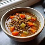 Close-up of a hearty bowl of lentil soup filled with brown lentils, diced carrots, and celery.