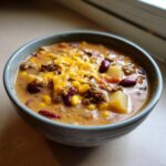 Close-up of a bowl of hearty cowboy soup filled with ground beef, corn, kidney beans, potatoes, and shredded cheddar cheese.