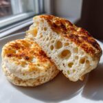 Close-up of a homemade English muffin split open, showing the airy interior texture and toasted surface.
