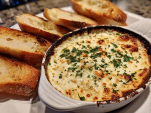 A bubbling, cheesy baked bread dip topped with parsley, served with toasted baguette slices for dipping.