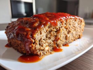 Close-up of a thick slice of juicy meatloaf topped with a sweet, dripping glaze.