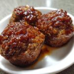 Three perfectly baked mini meatloaf portions topped with a shiny, dark brown glaze served in a white bowl.