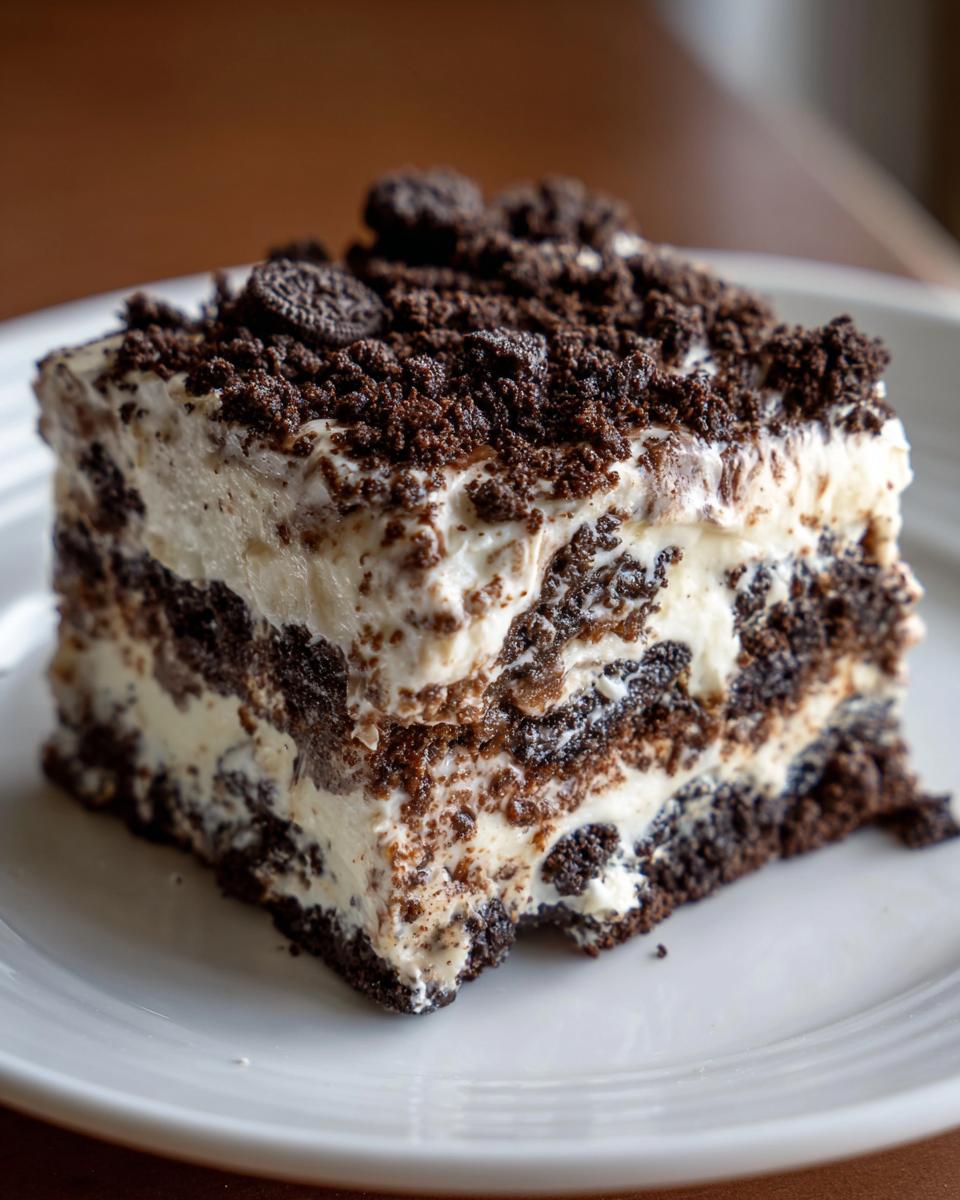 Close-up of a layered slice of oreo dirt cake with cream and crushed cookies.