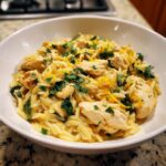 Close-up of creamy lemon chicken orzo pasta mixed with spinach, topped with fresh parsley and lemon zest.
