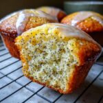 Close-up of a lemon poppy seed muffin cut in half showing the moist crumb filled with poppy seeds and topped with a lemon glaze.