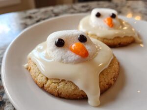 Two melted snowman cookies featuring a marshmallow head, white icing drip, and candy eyes/nose, ready to eat.