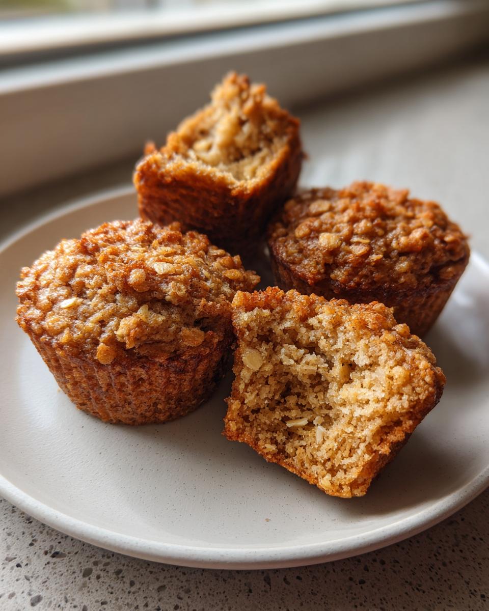 Four moist banana oatmeal muffins, one cut in half showing the texture, served on a light plate.