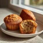 Three moist banana oatmeal muffins on a plate, one is broken open showing the texture inside.