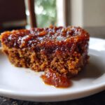 Close-up of a moist, dark cake slice generously topped with a shiny, thick layer of homemade pear butter.