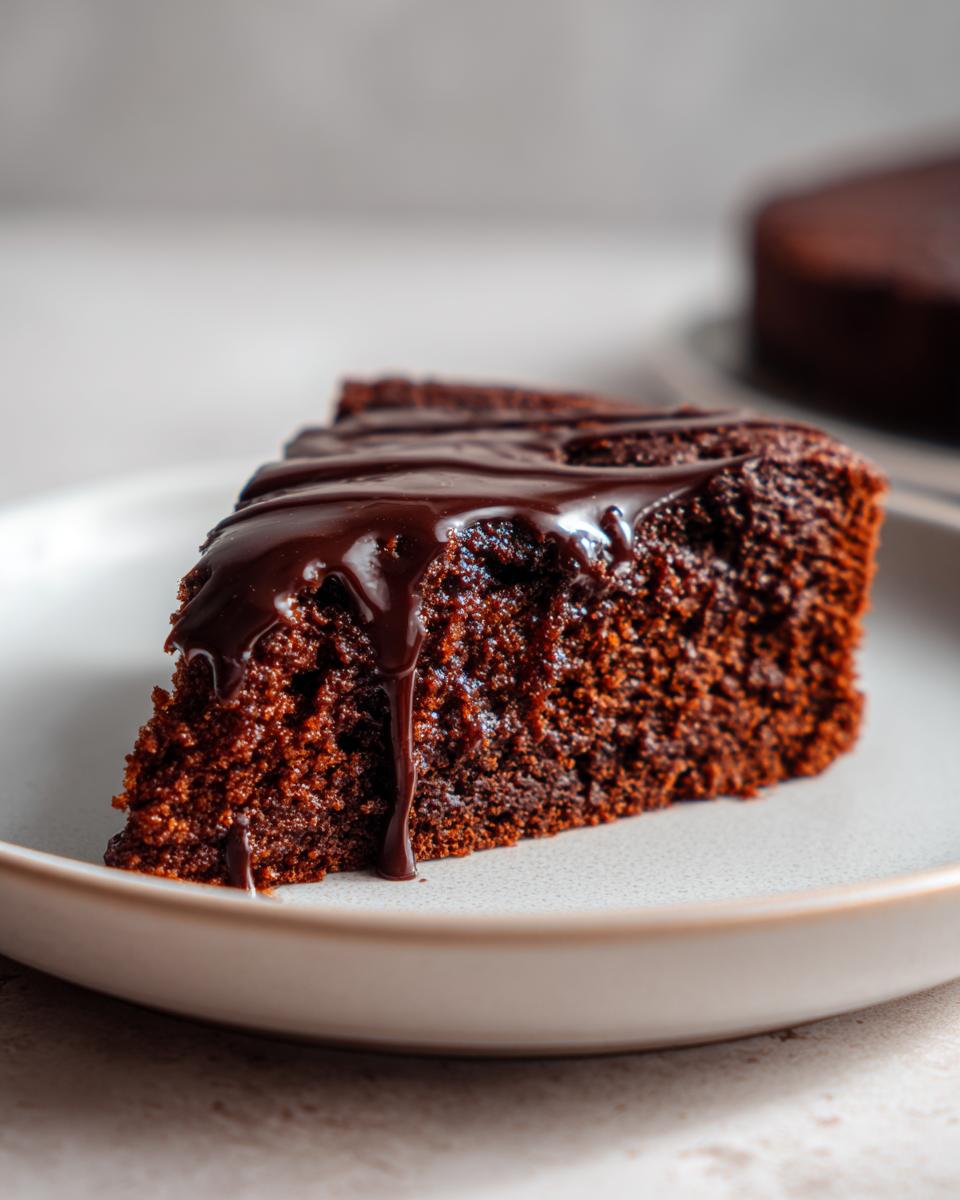 Close-up of a moist slice of dark gingerbread cake topped with rich, dripping chocolate glaze.