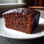 Close-up of a moist, dark slice of gingerbread cake topped with a shiny, thick caramel-like glaze.