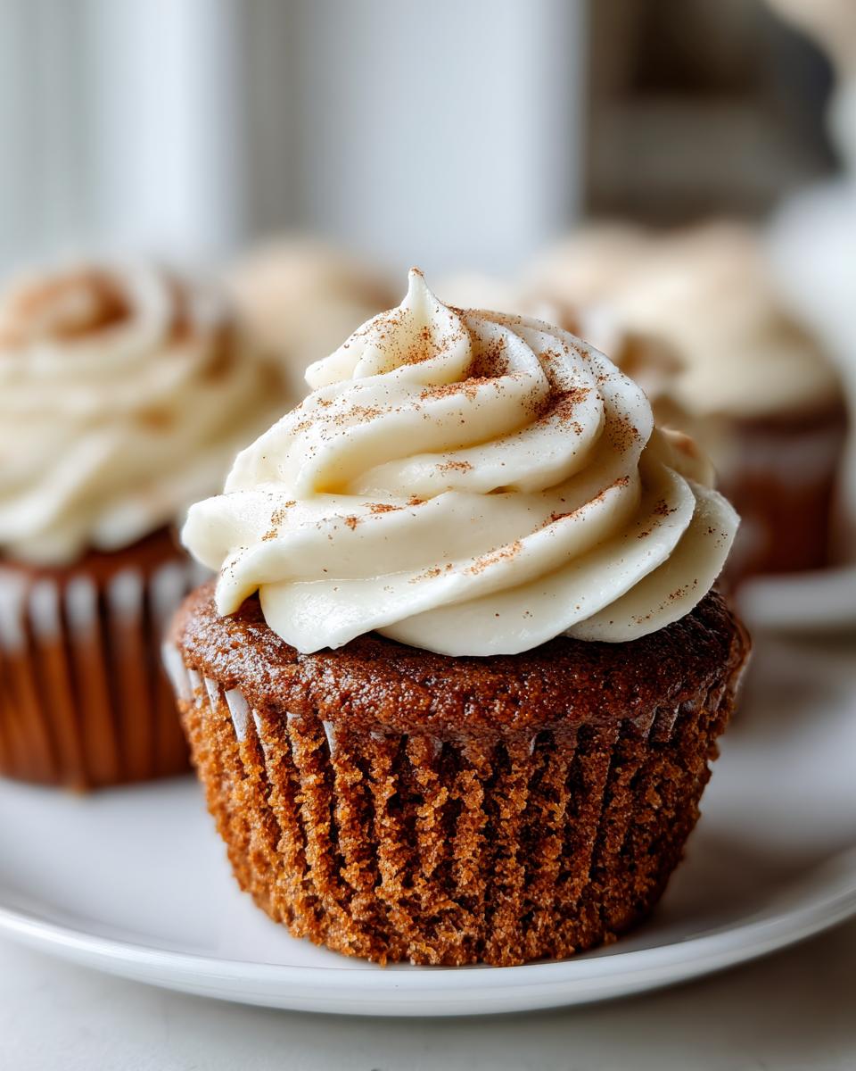A close-up shot of a moist gingerbread cupcakes topped with a swirl of cream cheese frosting dusted with cinnamon.