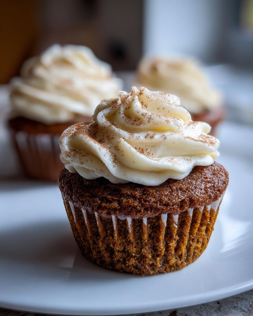 A close-up of one moist gingerbread cupcake topped with swirled cream cheese frosting and a dusting of cinnamon.