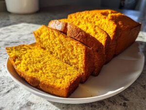 Close-up of several thick slices of vibrant orange moist pumpkin bread arranged on a white platter.
