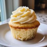Close-up of a single, moist vanilla cupcake topped with a generous swirl of light yellow vanilla buttercream frosting.