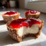 A close-up of a no-bake cheesecake bites with a bite taken out, showing the creamy filling and bright red strawberry topping.