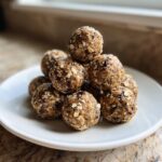 A pyramid stack of homemade protein balls made with oats and dark specks, served on a white plate.