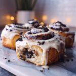Close-up of gooey Oreo cinnamon rolls topped with white icing and crushed cookies.