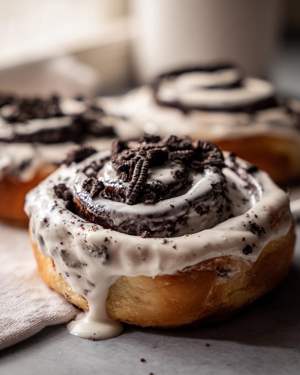 A close-up, decadent shot of one of the Oreo cinnamon rolls, heavily frosted and topped with crushed Oreo pieces.