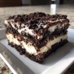 A thick, layered slice of rich Oreo dirt cake featuring dark chocolate crumbs and creamy white filling.
