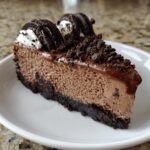A decadent slice of chocolate cheesecake with a dark crust, topped with chocolate ganache, whipped cream, and Oreo cookies.