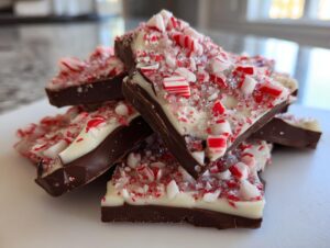 A stack of homemade peppermint bark recipe pieces showing dark chocolate, white chocolate, and crushed candy canes.
