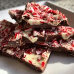 Close-up of stacked chocolate pieces from a peppermint bark recipe, topped with white chocolate and crushed candy canes.