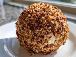 A close-up of a perfectly formed pineapple cheese ball coated entirely in chopped, toasted nuts.