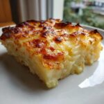 A close-up slice of creamy potatoes au gratin showing layered potatoes and a deeply browned, cheesy crust.