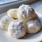A stack of soft, round lemon cookies heavily dusted with white powdered sugar on a white plate.