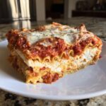 A thick, layered slice of ravioli lasagna with ricotta cheese, marinara sauce, and melted mozzarella topping.