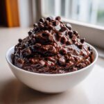 A close-up of rich, thick brownie batter dip piled high in a white bowl and generously topped with mini chocolate chips.
