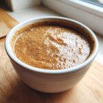 Close-up of rich, brown chicken gravy served in a small white bowl on a wooden surface.