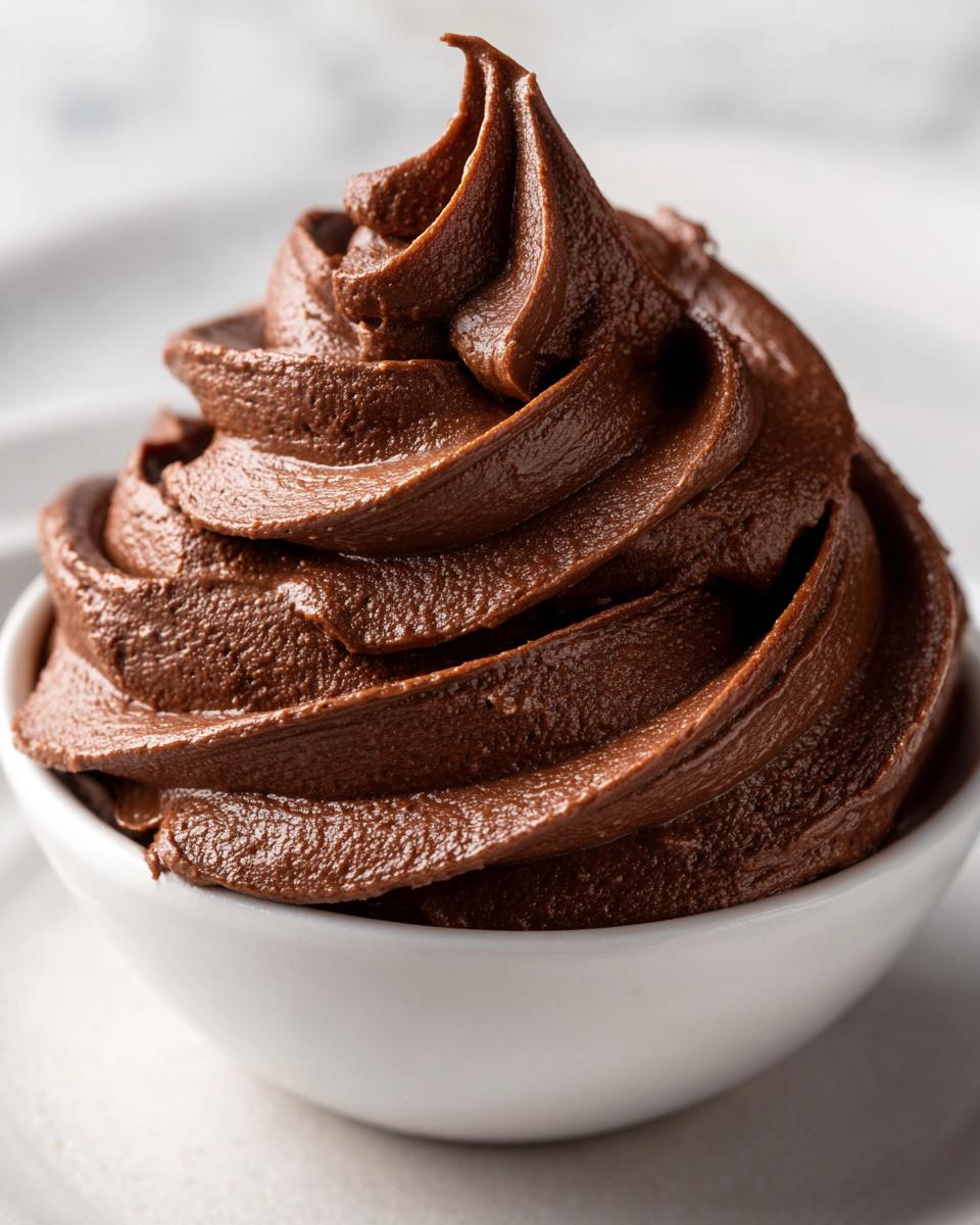 Close-up of rich, dark chocolate frosting piped into a perfect swirl inside a small white bowl.