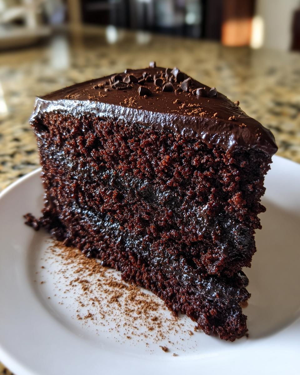 Close-up of a rich, dark slice of capricorn cake covered in glossy chocolate ganache and chocolate chips.