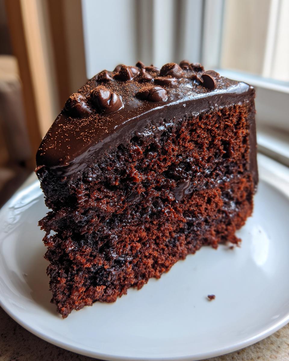 A moist, dark slice of rich capricorn cake topped with glossy chocolate ganache and chocolate chips.