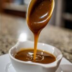 Close-up of rich, brown turkey gravy being poured from a spoon into a white gravy boat.