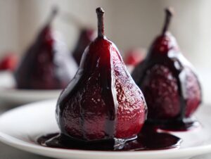A close-up of glistening, deep red poached pears drizzled with dark syrup on a white plate.