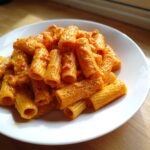 Close-up of rigatoni pasta coated in a rich, orange butternut squash pasta sauce, seasoned with pepper.