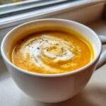 Close-up of vibrant orange roasted butternut squash soup topped with a swirl of cream and cracked black pepper.