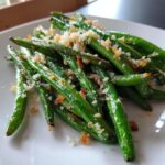 Close-up of bright green roasted green beans topped with crispy breadcrumbs or salt.