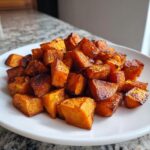 A pile of perfectly caramelized roasted sweet potato cubes served on a white plate.