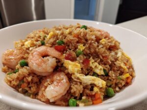Close-up of a white bowl filled with flavorful shrimp fried rice, featuring large pink shrimp and scrambled egg pieces.