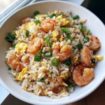 Close-up of a white bowl filled with delicious shrimp fried rice recipe, featuring plump shrimp, scrambled egg, and green onions.