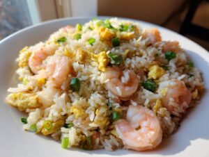 Close-up of a generous serving of shrimp fried rice recipe with pink shrimp, scrambled egg pieces, and green onions.