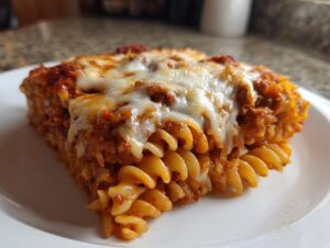 Close-up of a square slice of pizza casserole made with rotini pasta, covered in rich tomato sauce and melted mozzarella cheese.