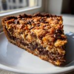 A close-up slice of rich, layered texas trash pie topped with crunchy streusel and chocolate chips.